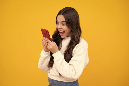 Cute teen child girl paying with phone, texting and chatting on smartphone. Excited teenager girl.の写真素材