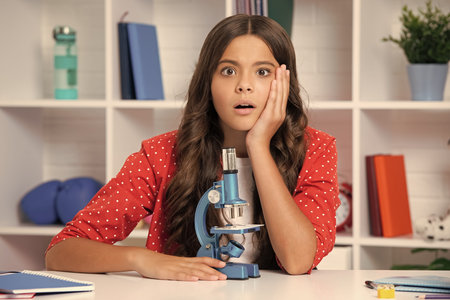 School girl with microscope for school education at home. Surprised face, surprise emotions of...