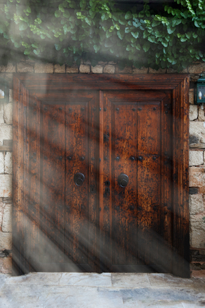 Old vintage wooden double doors with iron handles, sun rays on the left sideの写真素材