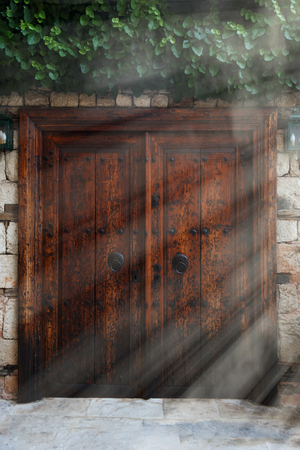 Old vintage wooden double doors with iron handles, sun rays on the right sideの写真素材