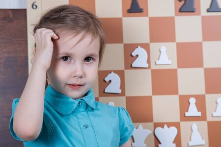 Playing chess on the demo board. Girl with braids in a pink suit, playing with white pieces on a...