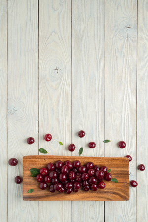ripe cherries and leaves in a wooden plate on a textured wooden background, view from aboveの写真素材