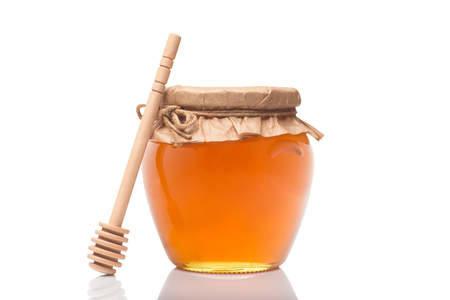Glass jar full of honey and wooden stick on it isolated on a white backgroundの写真素材
