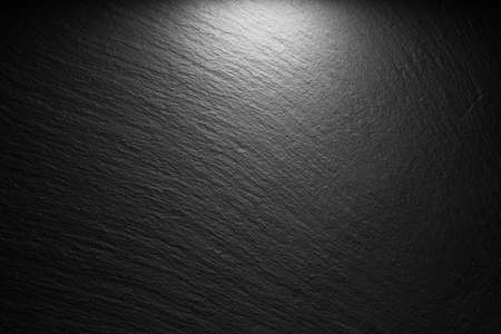 textured black slate background with spot of lightの写真素材