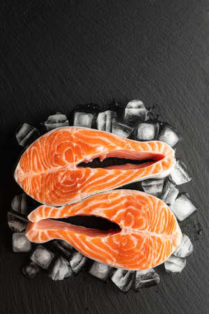 chilled salmon steak and ice on a stone background, top view, place for textの写真素材