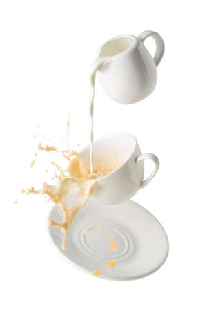 pouring milk and splashing milk tea from flying cup and saucer isolated on white backgroundの写真素材