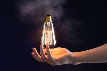 hand holds in the air a burning vintage light bulb without wiresの写真素材