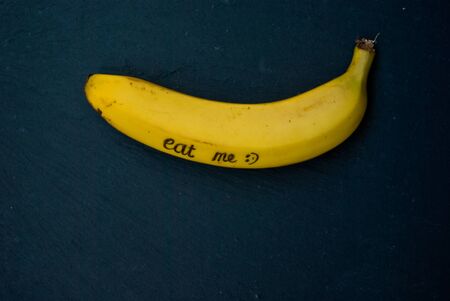 single ripe yellow banana laying on black background with writing "eat me" and copy spaceの写真素材