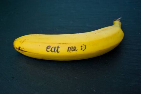 ripe  single yellow single banana on a black  stone table with writing "eat me"の写真素材