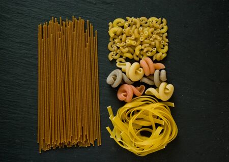 assortment of variety of italian uncooked pasta flat lay on a black stone background with copy spaceの写真素材