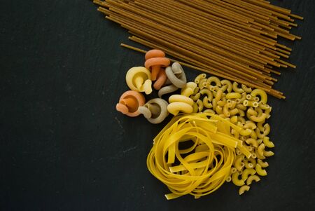 assortment of variety of italian uncooked pasta flat lay on a black stone background with copy spaceの写真素材