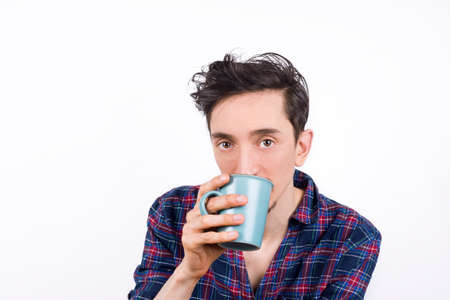Isolated portrait of a man wearing pajamas and drinking his morning coffee, looking into the camera.