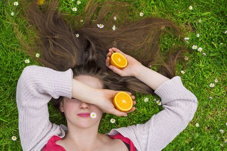 young woman laying on a grass field holding orangesの写真素材