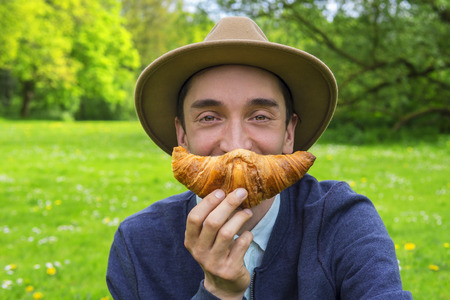 Stylish man eating a croissant outdoorsの写真素材