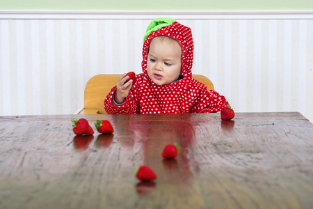 cute baby in berry suit eating strawberriesの写真素材