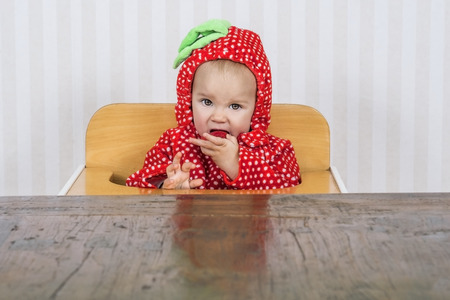 Adorable baby in strawberry suit eating a strawberryの写真素材