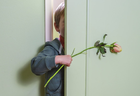 little kid hiding behind the door and holding a flowerの写真素材
