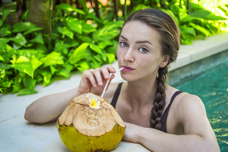 Young woman in swimming pool with a fresh coconutの写真素材