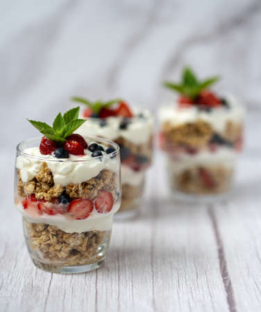Glass with granola, yogurt, fresh strawberries and blueberrys on white table. Healthy breakfast bowl concept.の写真素材