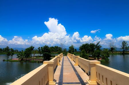 The long bridge is the way to the island, with green trees and white clouds and beautiful blue sky behind.の写真素材