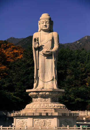 A large white Buddha standing, with mountains and sky in the background.の写真素材