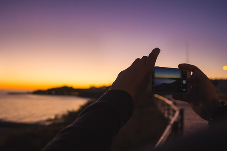 Taking picture of purple sunset at ocean with mobile phoneの写真素材