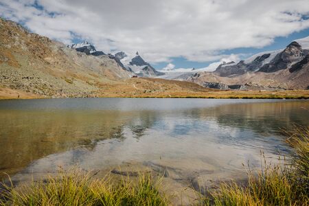 Small red tourists shelter house and beautiful mountains lake with snowy peaks of Swiss Alps reflectionの写真素材