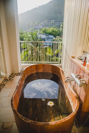 Brown wooden bath tub full with water on the balcony with picturesque view on green jungles forest of palm trees in Ao Nang village in Krabi province, Thailandの写真素材