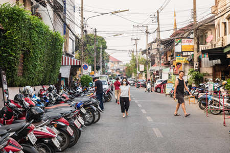 Chianf Mai, Thailand - February 9, 2020: Woman in black mask walking on street full of motorbikes in touristic Chiang Mai town in Northern Thailandのeditorial素材