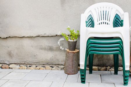 Stack of plastic chairs near old textured wall in garden countryside