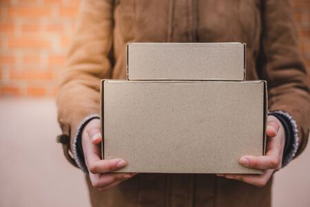 Person in brown coat holding two simple paper carboard packages from deliveryの写真素材