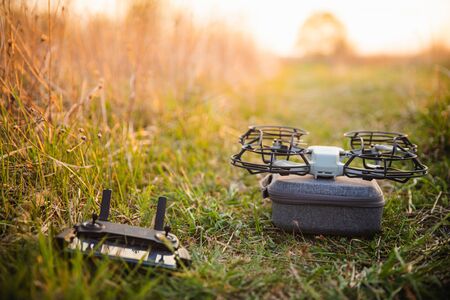 Small drone with propeller guard on grey case with control phone on green frass in summer field with warm sunset lightの写真素材