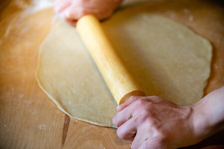 Hands on brown rolling pin with small white dough and wheat flour on wooden slab worktopの写真素材