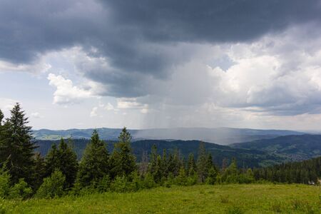 Shower rain and dark stormy clouds sky ove grass on green summer pasture with wooden fence on farm...