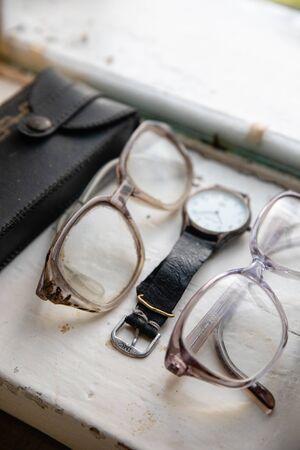 Old glasses and retro watch on white background near windowの写真素材