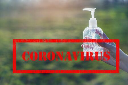 Corona virus red sign and transparent white plastic bottle of antibacterial sanitizer fluid in hands with clear green background with lightの写真素材