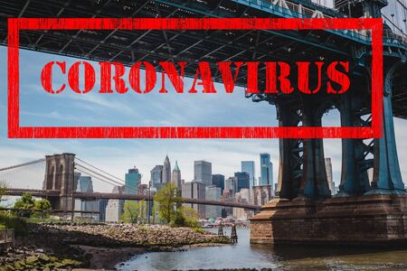 Coronavirus in New York, corona virus covid-19 red stamp sign on Manhattan Bridge and view on New York downtown, cityscape of Manhattan, USAの写真素材