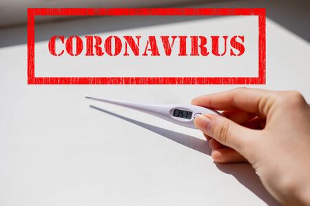 Coronavirus sign stamp and white electronic thermometer in hand showing low temperature with white...