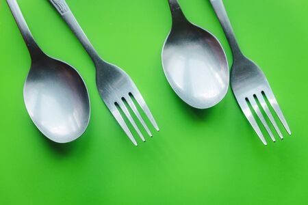 Metal forks and spoons cutlery on green background flat layの写真素材