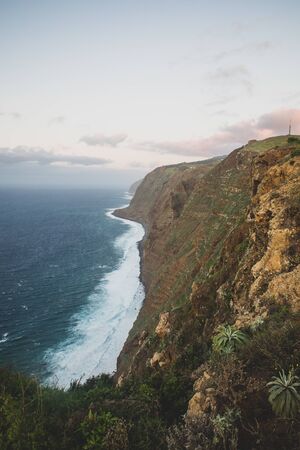 Beautiful scenic sunset view on cliffs coast of Atlantic Ocean with blue breaking waves in Madeira islandの写真素材
