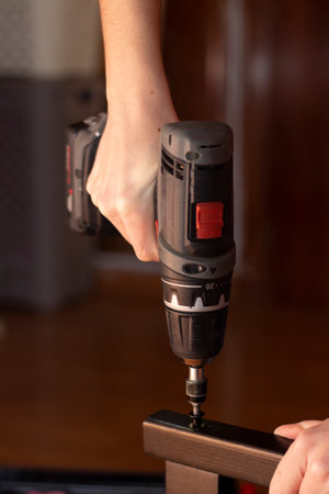 a electric drill assembles a brown wood chair with a screwの写真素材