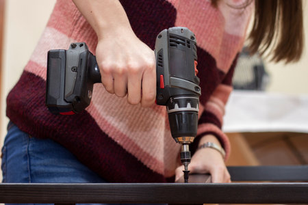 a kneeling girl with a drill electric drilling a wooden piecesの写真素材