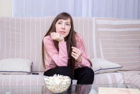 worried woman while watching television with a bowl popcorn on the tableの写真素材