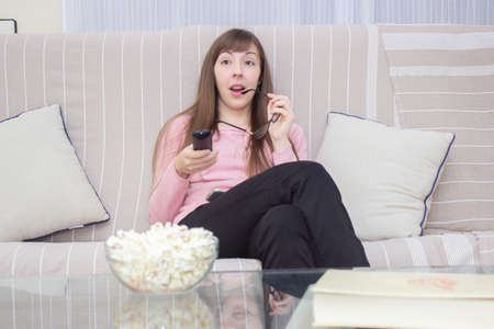 surprised woman watching television with a bowl popcorn on the tableの写真素材