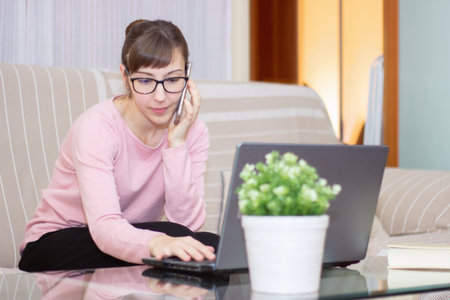 woman working with her computer while talking on phoneの写真素材