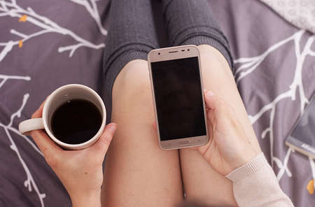 a woman looking at her mobile phone and drinking black coffeeの写真素材
