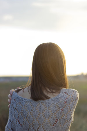 a young woman looking at the sunset and touching her shoulder in the field