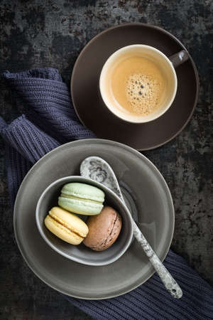 Colourful macarons in a small cup with y cup of coffeeの写真素材