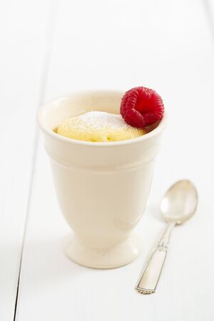 Vanilla mug cake with powdered sugar and a raspberry in beige mug with silver spoonの写真素材