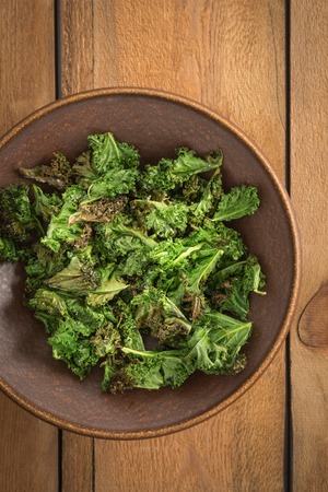 Kale chips with sea salt in a brown bowl on a wooden tableの写真素材
